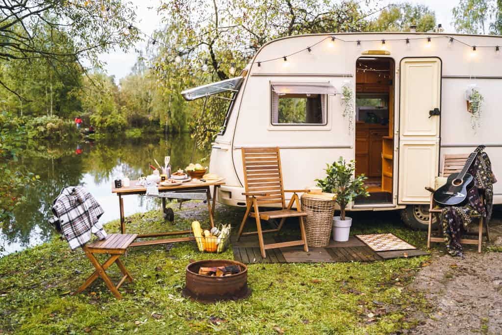 A camper set up along a creek with a picnic table and chair