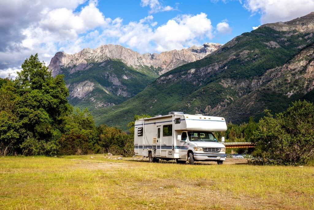 A large RV parked in a field with beautiful mountains in the background and a blue sky