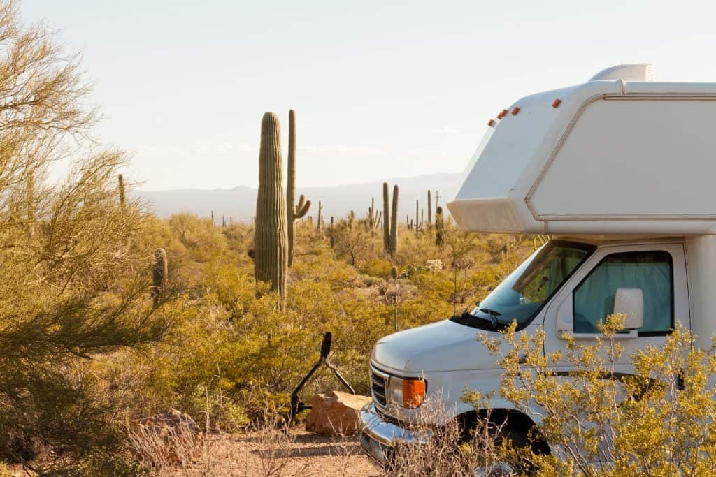 The front of an RV and series of cacti behind it in a desert